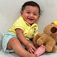 Gabriel joined the competition — help win amazing prizes! baby, child, smiling, yellow_shirt, striped_shorts, teddy_bear, plush_toy, barefoot, sitting, happy, cute, indoor, portrait, infant, playful, hand_touching_foot, soft_texture, light_background, young, person