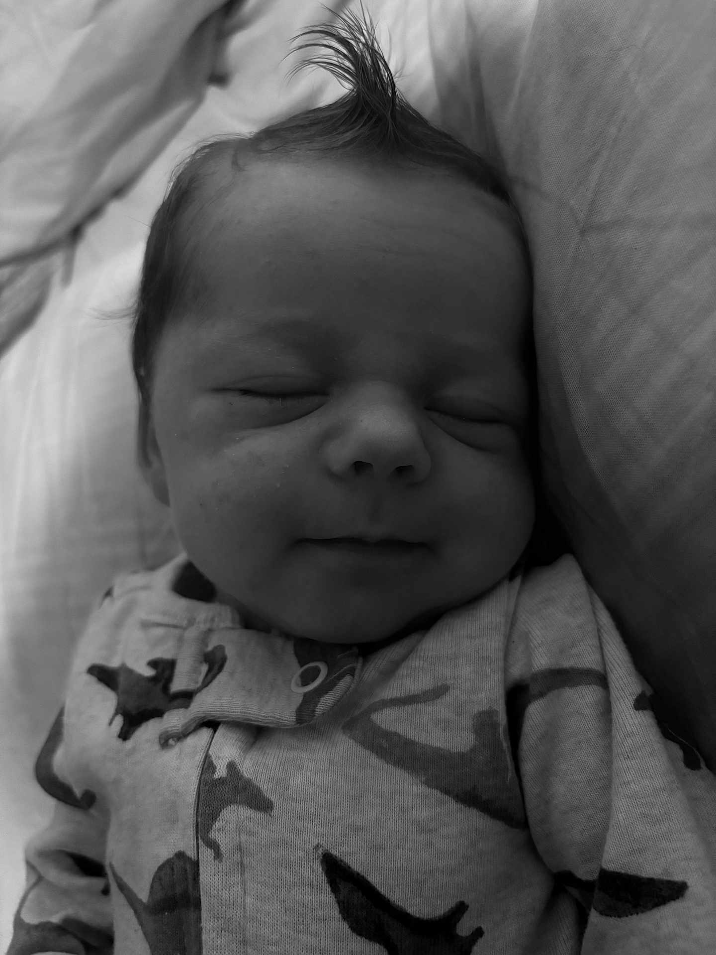 Colton joined the competition — help win amazing prizes! baby, sleeping, infant, face, hair, onesie, dinosaur_pattern, cozy, bed, pillow, blanket, cute, peaceful, newborn, portrait, child, soft_lighting, monochrome, closeup, resting