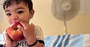 Faivish is registered to the contest to win money with this photo: apple, bed, bite, blanket, bracelet, child, clothing, cute, face, fan, furniture, happy, home, indoor, person, playful, portrait, sitting, toddler, young_child