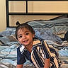 toddler, child, smiling, bed, striped_shirt, crawling, indoor, hair_tie, happy, person, cute, young_child, home, plaid_bedspread, casual_clothing, portrait, baby, fun, comfort, playful