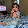toddler, child, smiling, bed, blanket, striped_bedding, indoor, window, blinds, television, cartoon, snack, happy, person, short_hair, clothing, sitting, foot, home, cozy