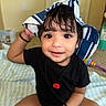 Faivish is registered to the contest to win money with this photo: accessory, big_eyes, black_shirt, blanket, child, cross_legged, curly_hair, cute, floor, happy, home, indoors, person, playful, sitting, smiling, striped_hat, toddler, toy, young_child