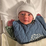 Livio participe au concours pour gagner de l'argent avec cette photo : baby, infant, hat, knit_hat, blue_bib, blanket, cozy, wide_eyes, curious, soft_texture, newborn, cute, child, lying_down, indoors, clothing, warm, hands, face, portrait