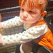 Alessandra joined the competition — help win amazing prizes! toddler, child, red_hair, pigtails, white_top, orange_dress, curious, indoor, restaurant, metal_grid, leaning, baby, person, cute, expression, seat, wooden_floor, clothing, face, portrait