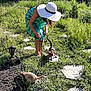 person, ferret, leash, garden, grass, stone_path, sunhat, dress, plants, outdoor, daylight, greenery, wildflowers, pet, nature, animal, summer, walking, curious, playful
