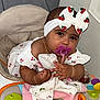 baby, baby_seat, bow, cherry_pattern, child, clothing, colorful, cute, dress, face, hands, headband, indoor, infant, pacifier, person, playful, sitting, stuffed_animal, toy