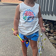 Anthony joined the competition — help win amazing prizes! toddler, child, barefoot, smiling, tank_top, shorts, pinwheel, plastic_bag, sidewalk, outdoor, happy, summer, playful, person, young_child, casual_clothing, daylight, curly_hair, cute, standing