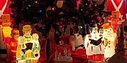 Oreo is registered to the contest to win money with this photo: christmas_tree, cat, holiday_lights, decorations, figurines, festive, indoor, black_and_white_cat, ornaments, red_tree_skirt, snowman, toy_soldier, carolers, santa_figurine, night, warm_lighting, cozy, celebration, festivity, holiday_scene