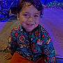 blue_lighting, casual, child, clothing, face, happy, jacket, marvel, night, outdoor, person, portrait, purple_lighting, sidewalk, sitting, smiling, stroller, superhero, wheel, young