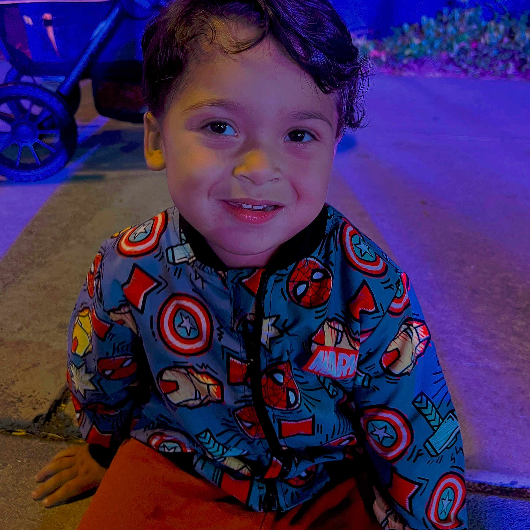 Shyloe joined the competition — help win amazing prizes! blue_lighting, casual, child, clothing, face, happy, jacket, marvel, night, outdoor, person, portrait, purple_lighting, sidewalk, sitting, smiling, stroller, superhero, wheel, young