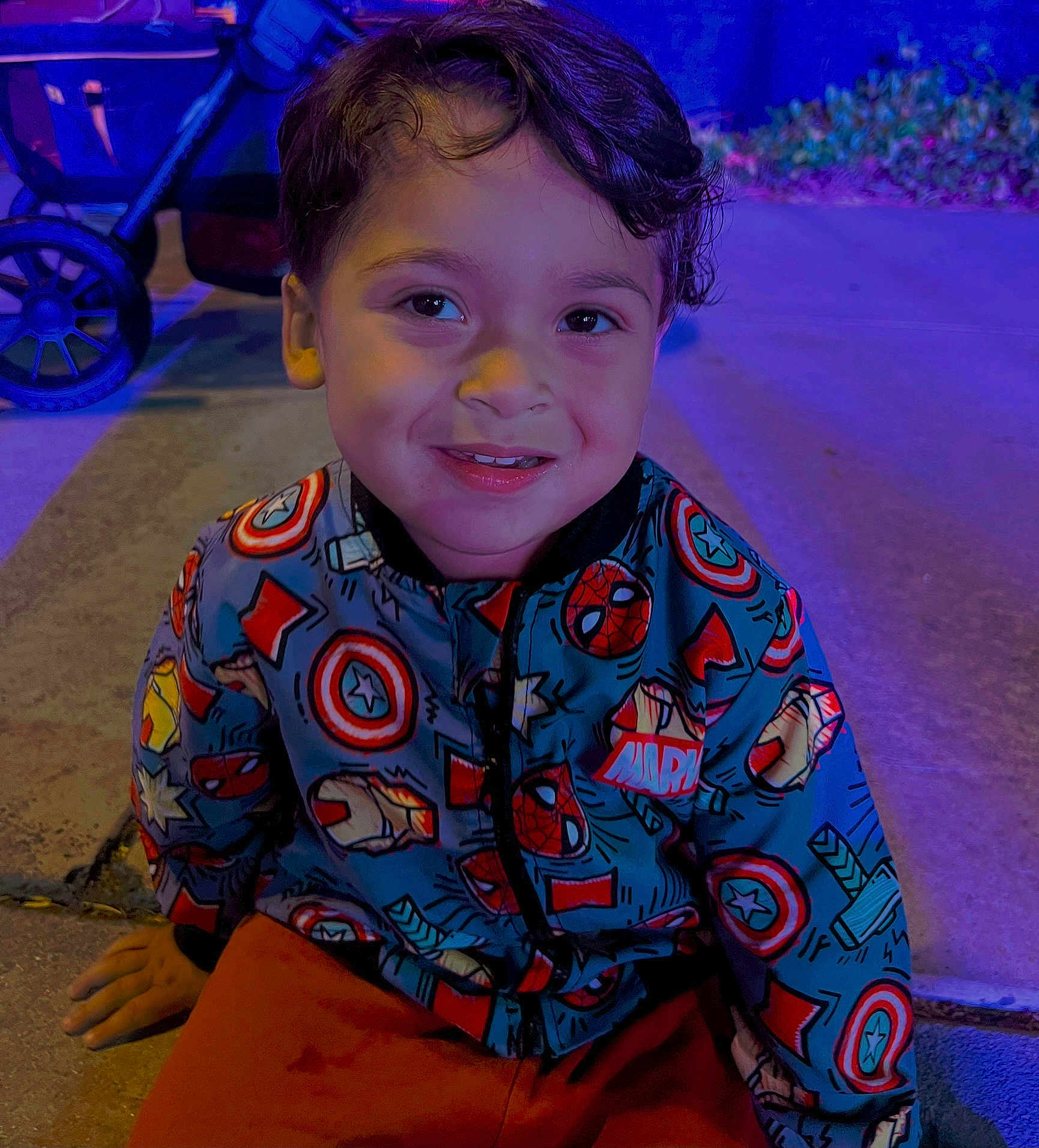 Shyloe joined the competition — help win amazing prizes! blue_lighting, casual, child, clothing, face, happy, jacket, marvel, night, outdoor, person, portrait, purple_lighting, sidewalk, sitting, smiling, stroller, superhero, wheel, young