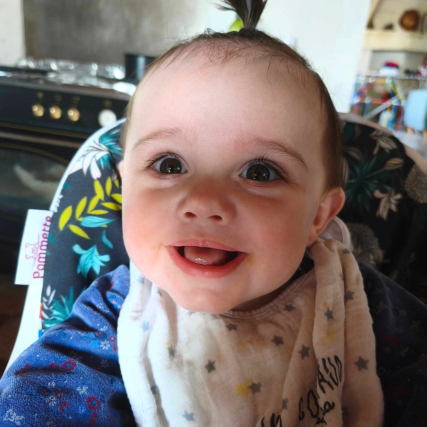 Maëlle participe au concours pour gagner de l'argent avec cette photo : baby, child, smiling, face, bib, hair, pony_tail, high_chair, clothing, indoor, kitchen, happy, portrait, person, cute, infant, closeup, apparel, young_child, expressive