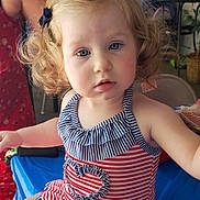 Adalena is registered to the contest to win money with this photo: toddler, child, curly_hair, blue_eyes, striped_swimsuit, red_and_white, navy_blue, ruffles, indoor, table, hand, person, face, sitting, cute, curious, skin, blonde_hair, baby, portrait