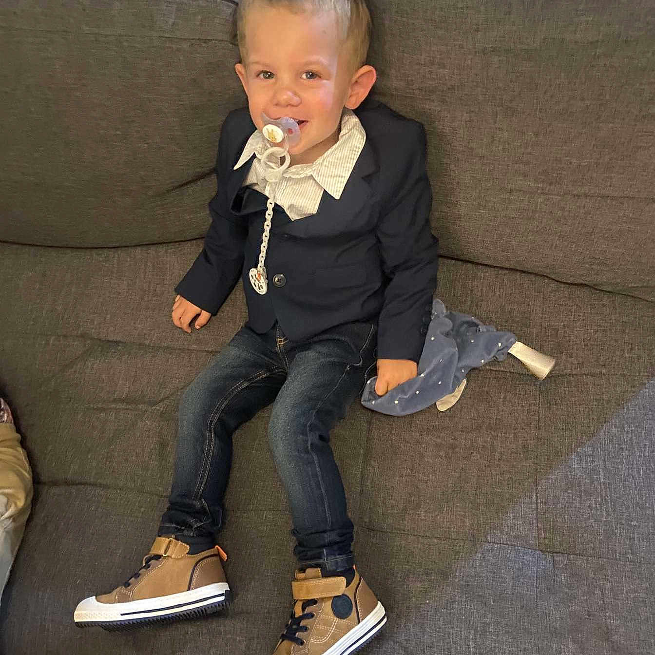 Mélyohann a rejoint le concours — aidez-le/la à gagner de superbes lots ! blanket, blazer, boy, casual_shoe, child, collared_shirt, couch, cute, indoor, jeans, living_room, pacifier, pacifier_clip, portrait, sitting, smile, sneakers, sofa, suit_jacket, toddler