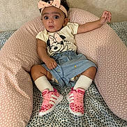 Maya participe au concours pour gagner de l'argent avec cette photo : baby, child, headband, pink, sneakers, socks, denim_shorts, tshirt, minnie_mouse, cushion, patterned_background, curious_expression, indoor, seated, person, footwear, clothing, soft_furniture, infant, cute