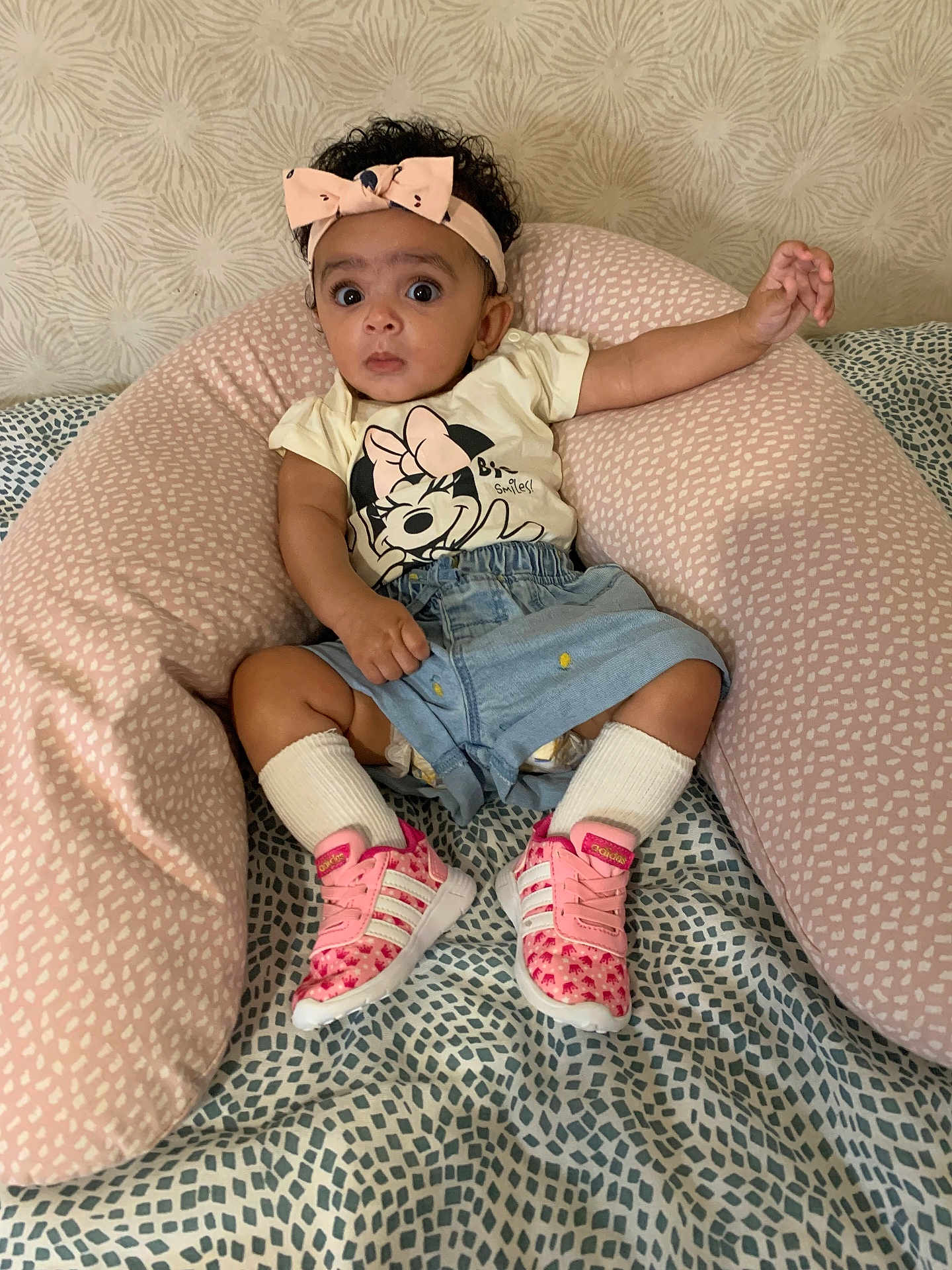 Maya participe au concours pour gagner de l'argent avec cette photo : baby, child, headband, pink, sneakers, socks, denim_shorts, tshirt, minnie_mouse, cushion, patterned_background, curious_expression, indoor, seated, person, footwear, clothing, soft_furniture, infant, cute