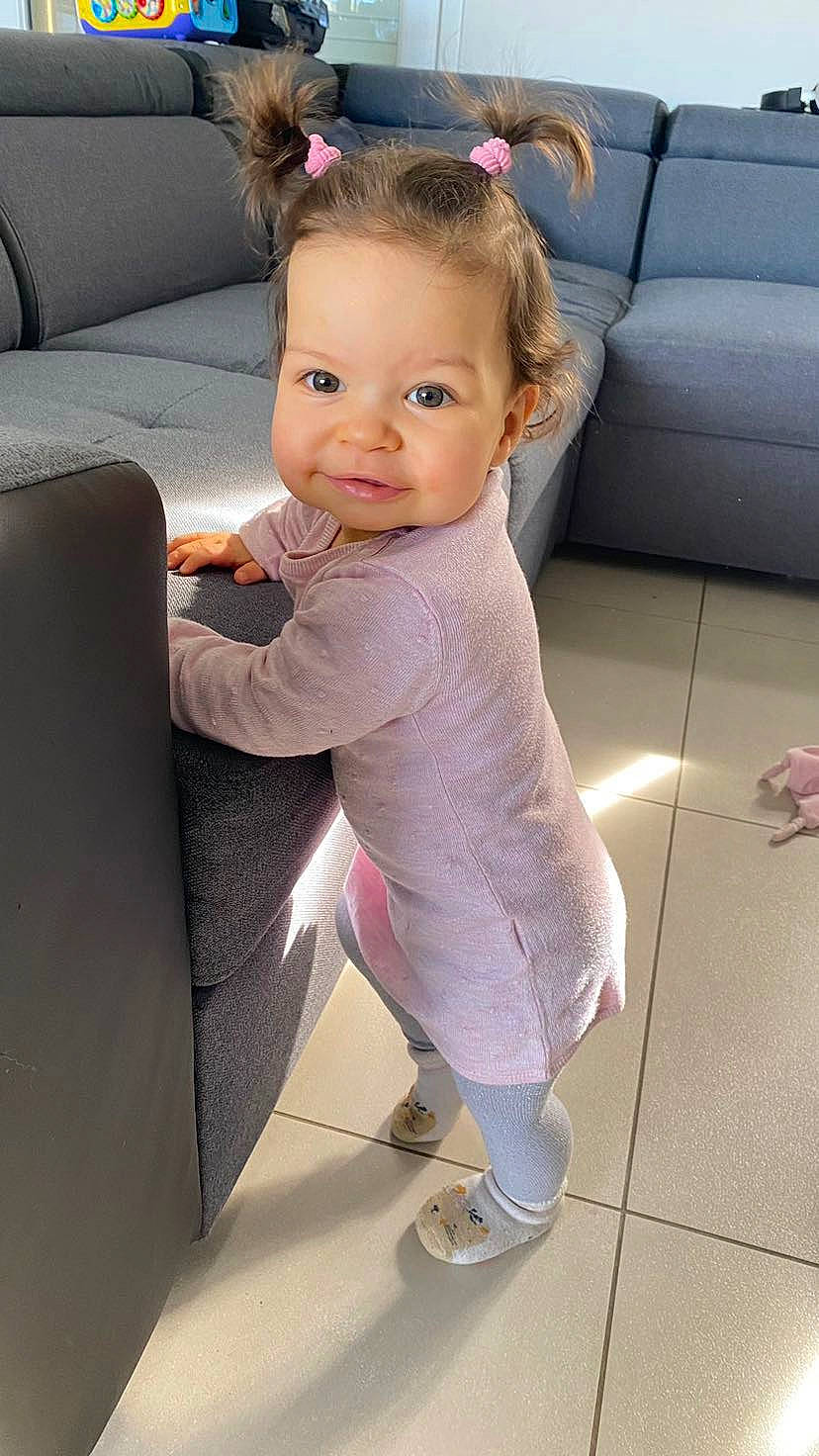 Illyana participe au concours pour gagner de l'argent avec cette photo : baby, baby_toddler_clothing, child, comfort, couch, floor, flooring, hair, happy, head, human_leg, leg, person, pink, purple, sandal, shoe, smile, sneakers, toddler
