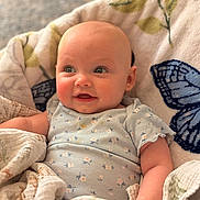 Riley joined the competition — help win amazing prizes! baby, infant, smile, blanket, onesie, floral_pattern, face, skin, head, cheeks, eyes, arm, hand, soft_texture, indoor, cozy, cute, child, person, portrait