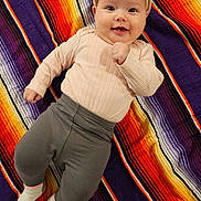 Alaina is registered to the contest to win money with this photo: baby, child, smiling, headband, blanket, striped_blanket, clothing, long_sleeve, pants, socks, cute, lying_down, indoors, portrait, happy, infant, face, young_child, colorful, soft_lighting
