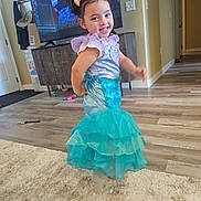 Juliette is registered to the contest to win money with this photo: child, girl, mermaid_costume, dress, smile, indoor, living_room, television, carpet, wood_floor, furniture, toy, pigtails, hair_bows, happy, playful, person, costume, home, cute