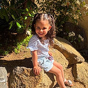Melyna participe au concours pour gagner de l'argent avec cette photo : child, girl, smile, pigtails, rock, outdoor, sunlight, plants, greenery, flowers, nature, summer, happy, sitting, shorts, striped_shirt, sandals, daylight, portrait, young