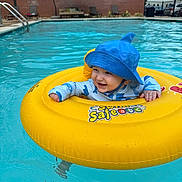 Leon is registered to the contest to win money with this photo: baby, child, pool, water, swim_ring, blue_hat, smiling, floating, summer, outdoor, swimming, fun, cute, yellow, safety, infant, playful, recreation, sunny, leisure
