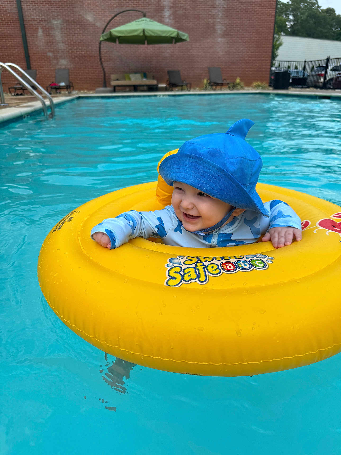 Leon is registered to the contest to win money with this photo: baby, child, pool, water, swim_ring, blue_hat, smiling, floating, summer, outdoor, swimming, fun, cute, yellow, safety, infant, playful, recreation, sunny, leisure