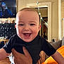 Leon is registered to the contest to win money with this photo: baby, smiling, child, person, indoor, hand, tattoo, black_shirt, striped_pants, couch, living_room, television, furniture, happy, face, skin, adult_hand, expression, home, holding