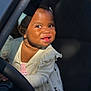toddler, child, smiling, face, headband, bow, dress, clothing, steering_wheel, car, vehicle_interior, happy, cute, young_child, portrait, human, baby, indoors, playful, curious