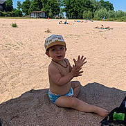 Tyago participe au concours pour gagner de l'argent avec cette photo : toddler, child, beach, sand, hat, cap, necklace, sitting, sunshine, shade, umbrella, outdoor, summer, nature, trees, people, relaxing, footwear, clothing, playful