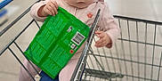 Milana participe au concours pour gagner de l'argent avec cette photo : toddler, child, shopping_cart, grocery_store, headband, pink_clothing, socks, green_packet, floor, metal_cart, shopping, baby, seat, cute, indoor, person, retail, blurred_background, exploring, curious