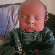Waylon is registered to the contest to win money with this photo: baby, newborn, infant, sleeping, closed_eyes, onesie, green_clothing, hand, face, cheeks, tuft_of_hair, couch, blanket, indoor, portrait, closeup, soft_lighting, adorable, relaxed, family