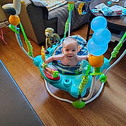 Elijah is registered to the contest to win money with this photo: baby, balloons, blanket, child, colorful, floor, furniture, happy, indoor, jumper, living_room, packaging, person, plastic, playtime, seat, smiling, table, toys, wooden_floor