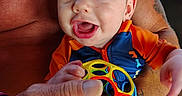 Elijah joined the competition — help win amazing prizes! adult, baby, bright, child, closeup, clothing, colorful, hand, happy, holding, infant, mesh_fence, outdoor, person, playful, portrait, skin, smiling, tattoo, toy