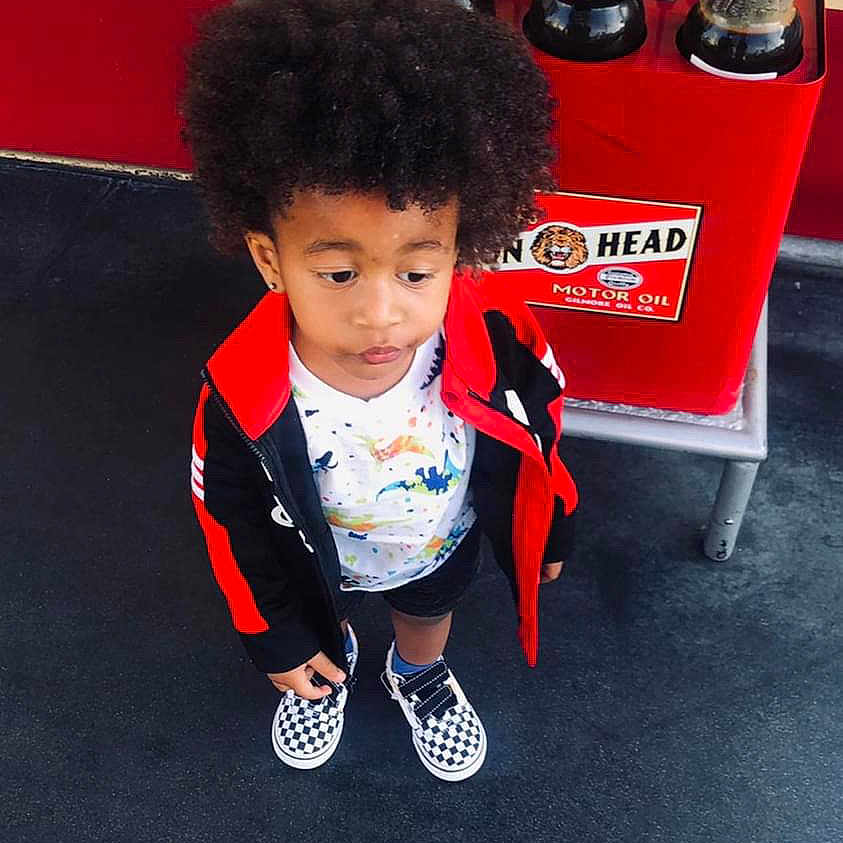 Zyaire is registered to the contest to win money with this photo: blackhair, boy, child, clothing, coat, curlyhair, face, footwear, hair, head, jacket, male, pants, person, photography, portrait, shoe, shorts, sitting, sneaker