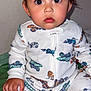 baby, child, onesie, clothing, sitting, indoor, face, wide_eyes, curious, bedspread, hand, infant, cute, portrait, young_child, colorful, patterned_clothing, person, closeup, expression
