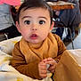 baby, child, blanket, high_chair, cafe, indoor, people, table, chair, face, hands, expression, clothing, person, drinks, blurred_background, curious, cute, warm_colors, family