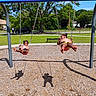 children, toddlers, siblings, playground, swings, swing_set, outdoor, park, sunny, summer, smiling, swinging, play, fun, chains, rubber_seats, wood_chips, trees, grass, neighborhood