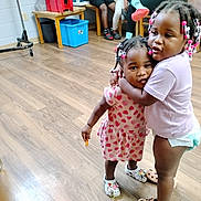 Ariya joined the competition — help win amazing prizes! children, siblings, girls, toddler, preschooler, hugging, portrait, smiling, indoors, classroom, wooden_floor, chairs, storage_bin, colorful_hair_beads, braids, pink_clothing, dress, diaper, clogs, candid_photo