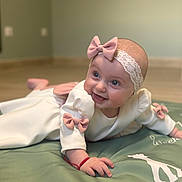 Noemie a rejoint le concours — aidez-le/la à gagner de superbes lots ! baby, infant, child, tummy_time, play_mat, pink_bow, headband, white_outfit, smile, happy, indoors, floor, wooden_floor, cute, portrait, person, crawling, red_bracelet, giraffe_print, soft_lighting