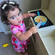 Kaia joined the competition — help win amazing prizes! toddler, child, toy, play_kitchen, pink_dress, curly_hair, spatula, toy_pan, pretend_play, indoor, carpet, barefoot, hair_clips, concentration, kitchen_toy_set, floor, young_girl, play_food, cute, home