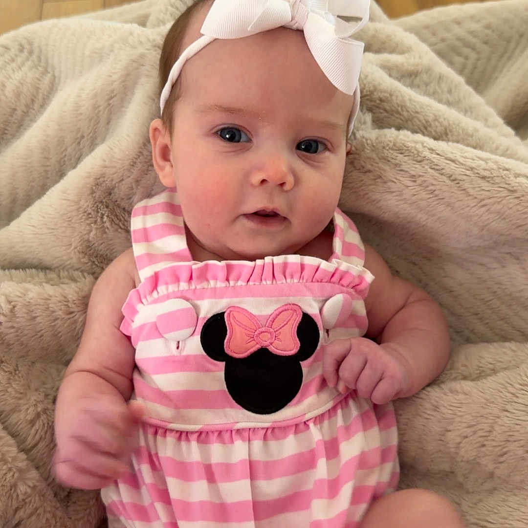 Carter Grace is registered to the contest to win money with this photo: baby, infant, headband, bow, pink_stripes, mickey_mouse, clothing, blanket, wooden_floor, cute, child, portrait, sitting, indoors, soft_texture, relaxed, young, small, person, adorable