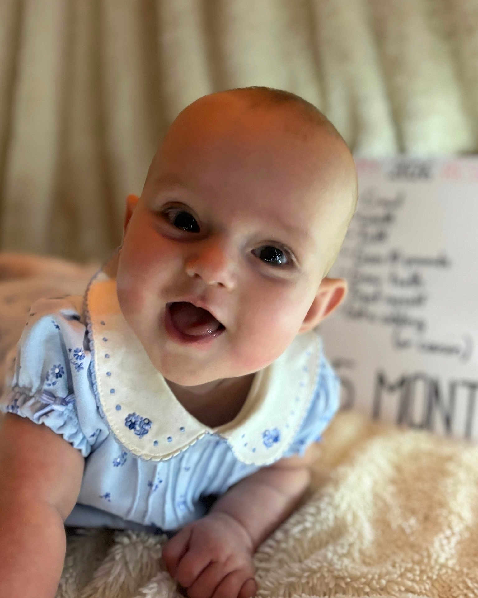 Oakley joined the competition — help win amazing prizes! baby, infant, smile, tongue_out, blue_dress, collar, cute, soft_blanket, closeup, face, child, happy, portrait, lying_down, indoors, skin, head, small_hand, expression, young
