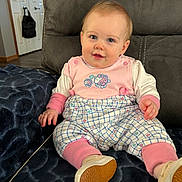 Ellie joined the competition — help win amazing prizes! baby, infant, child, sitting, pink_clothing, onesie, shoes, couch, blanket, blue_eyes, smile, portrait, home_interior, furniture, door, bag, hand, footwear, cozy, closeup