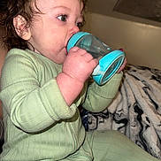 Oliver is registered to the contest to win money with this photo: toddler, child, baby, onesie, green_clothing, sippy_cup, curly_hair, drinking, indoor, blanket, closeup, cute, portrait, hand, face, sitting, soft_lighting, cozy, young_child, focused