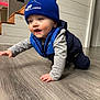 baby, crawling, blue_beanie, blue_vest, gray_sleeve, wooden_floor, indoor, stairs, ceiling_fan, happy, child, person, home, flooring, clothing, earrings, smiling, curious, infant, young_child