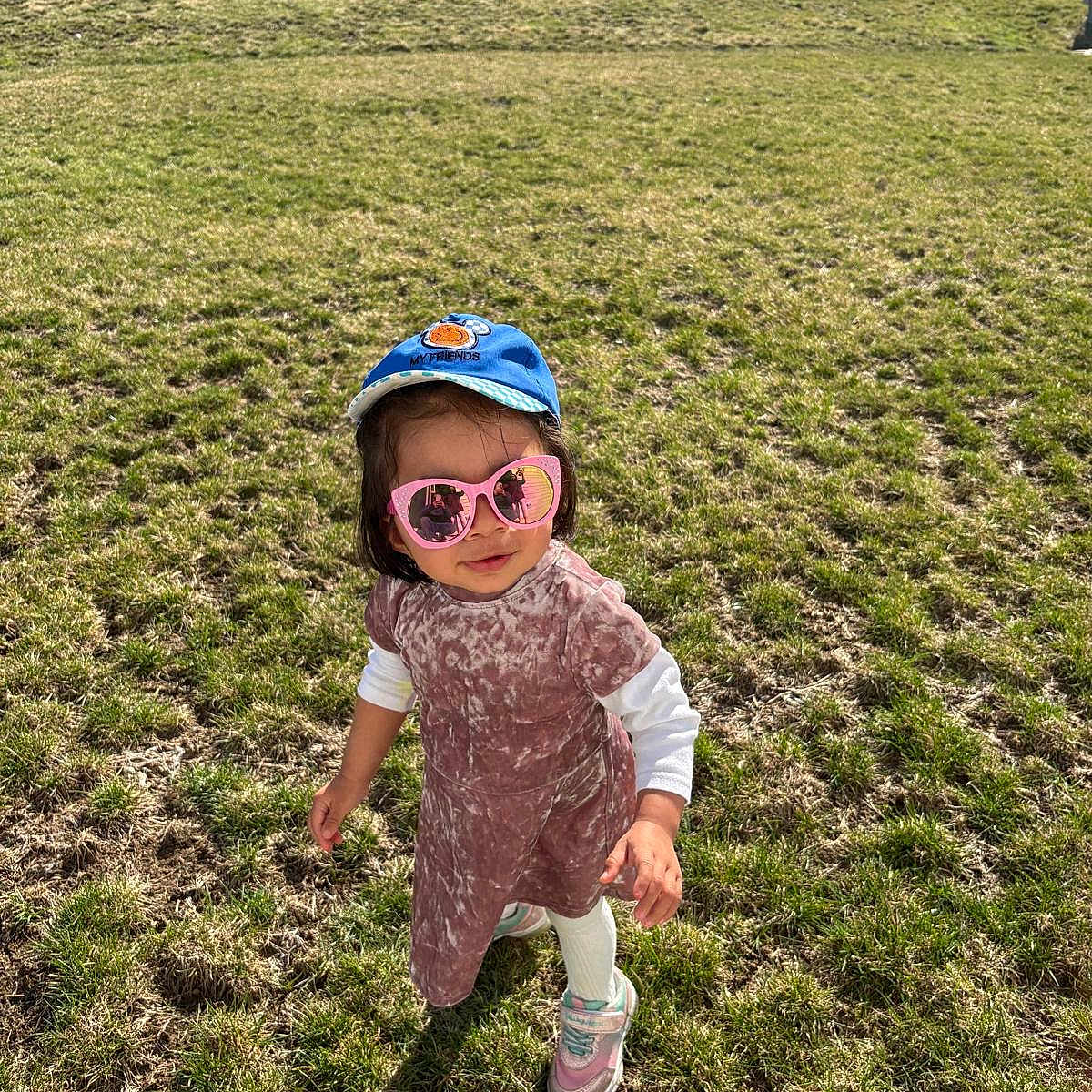 Shivanshi is registered to the contest to win money with this photo: toddler, child, grass, outdoor, sunglasses, cap, shadow, dress, shoes, sunny, yard, casual, person, fashion, walking, play, daylight, young, cute, summer