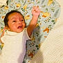 baby, infant, child, blanket, pattern, bird_pattern, clothing, onesie, lying_down, raised_arm, face, expression, hair, bed, striped_sheet, skin, person, newborn, cute, indoors