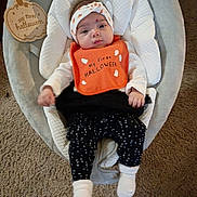 Khloe joined the competition — help win amazing prizes! baby, infant, halloween, bib, headband, baby_seat, carpet, clothing, socks, black_pants, white_shirt, orange_bib, wooden_sign, indoor, cute, looking_at_camera, soft_texture, festive, holiday, child
