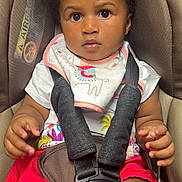 Edene participe au concours pour gagner de l'argent avec cette photo : baby, child, car_seat, seatbelt, bib, clothing, red_shorts, face, hands, infant, sitting, straps, safety, cute, young, portrait, indoor, person, expression, attention
